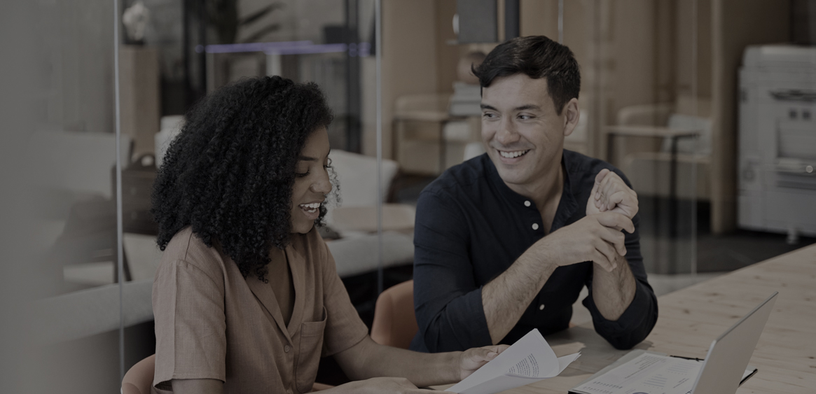 Two colleagues laughing while reviewing work at a desk