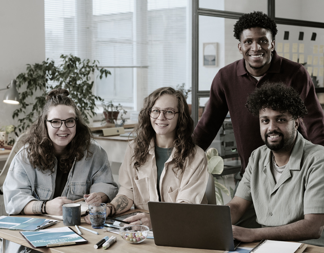 A team of four engineers smiling together at a laptop