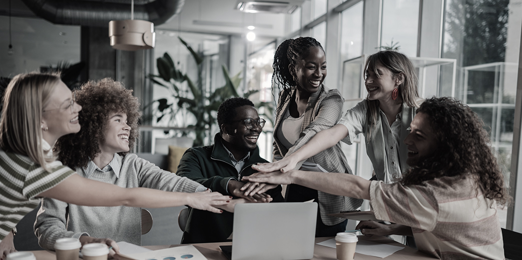 A diverse team stacking hands together over a laptop