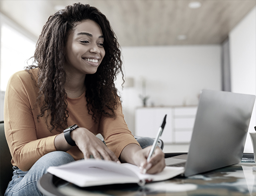 Smiling developer taking notes beside a laptop at home